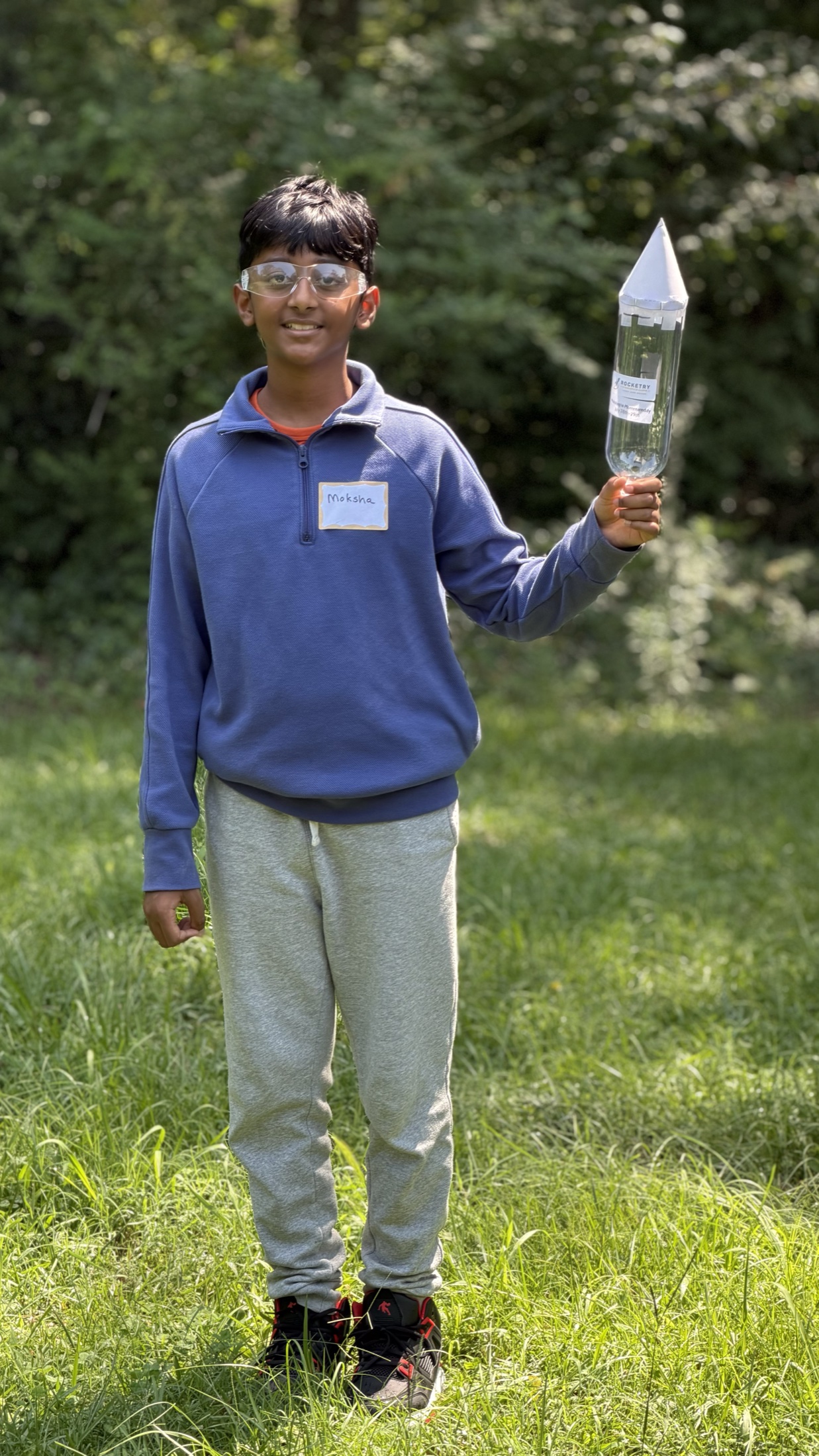 A student standing outdoors and proudly holding a completed bottle rocket