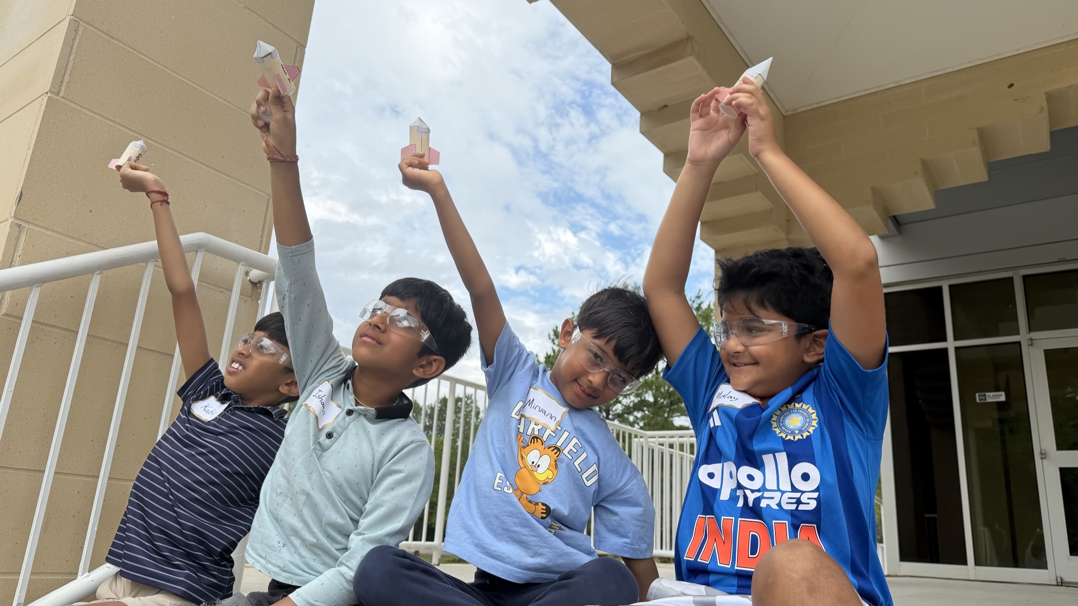 Four students celebrating with model rockets held overhead