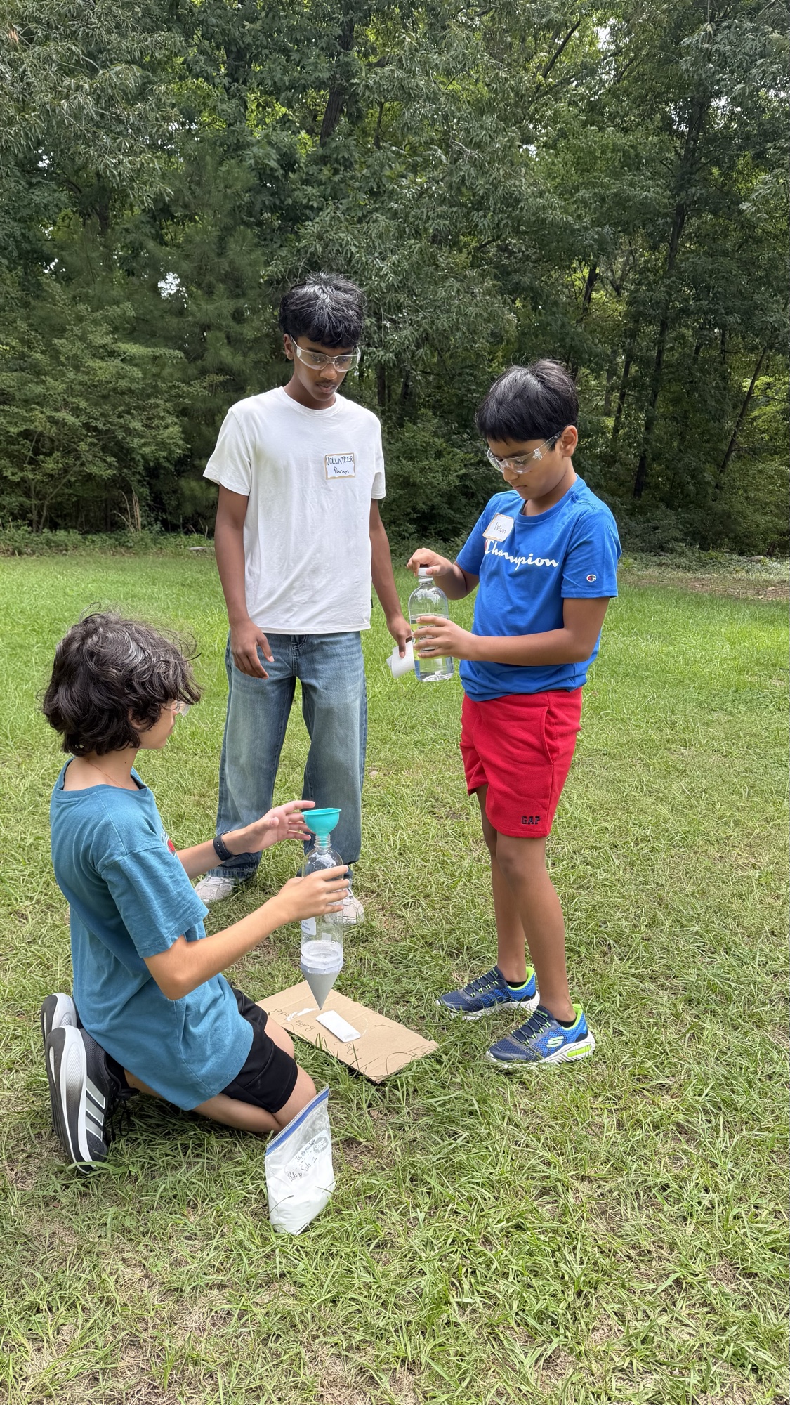Three students collaborating on bottle-rocket systems outdoors